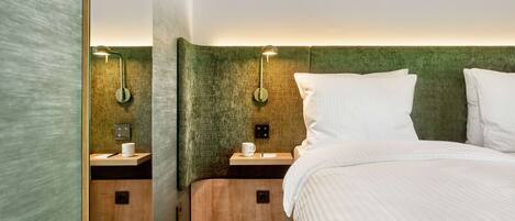 Een hotelkamer met een groot bed, twee nachtkastjes met lampen, een houten nachtkastje en een groen geweven hoofdeinde.