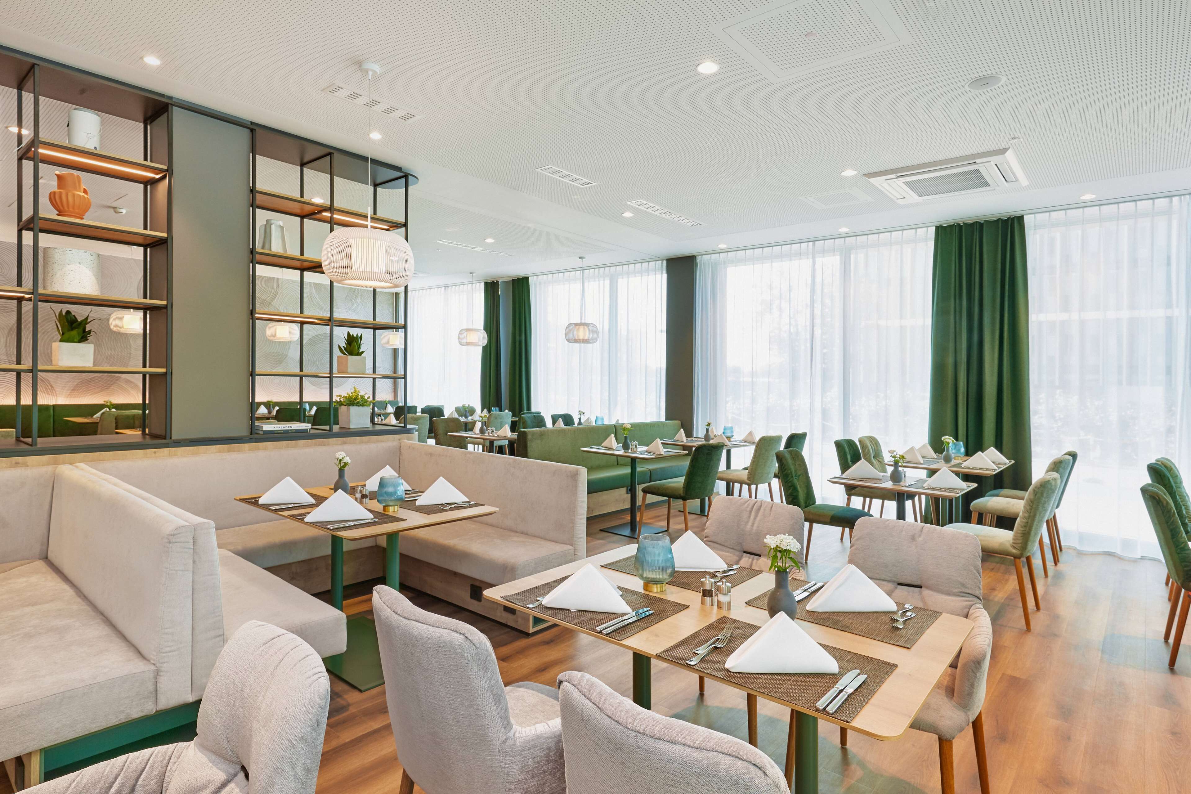 A modern restaurant with high tables, cushioned seating, and a green curtain backdrop.