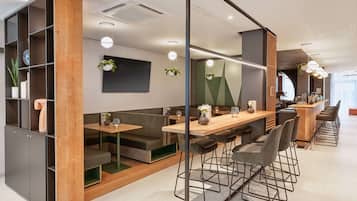 Un espacio de oficina moderno con una larga mesa común, taburetes tipo bar y un área de descanso con sofá y una mesa pequeña.