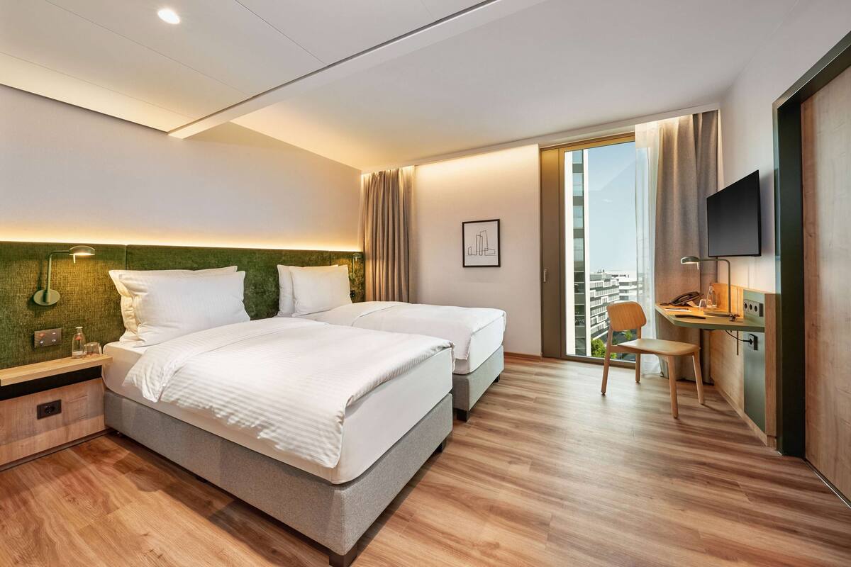 Ein Hotelzimmer mit einem großen Bett, einem Schreibtisch, einem Sessel, einem Fernseher und einem Fenster mit Vorhängen.