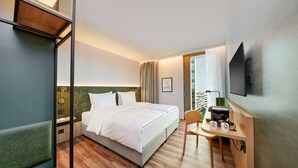 Habitación de hotel con cama, escritorio con cafetera y televisor montado en la pared.