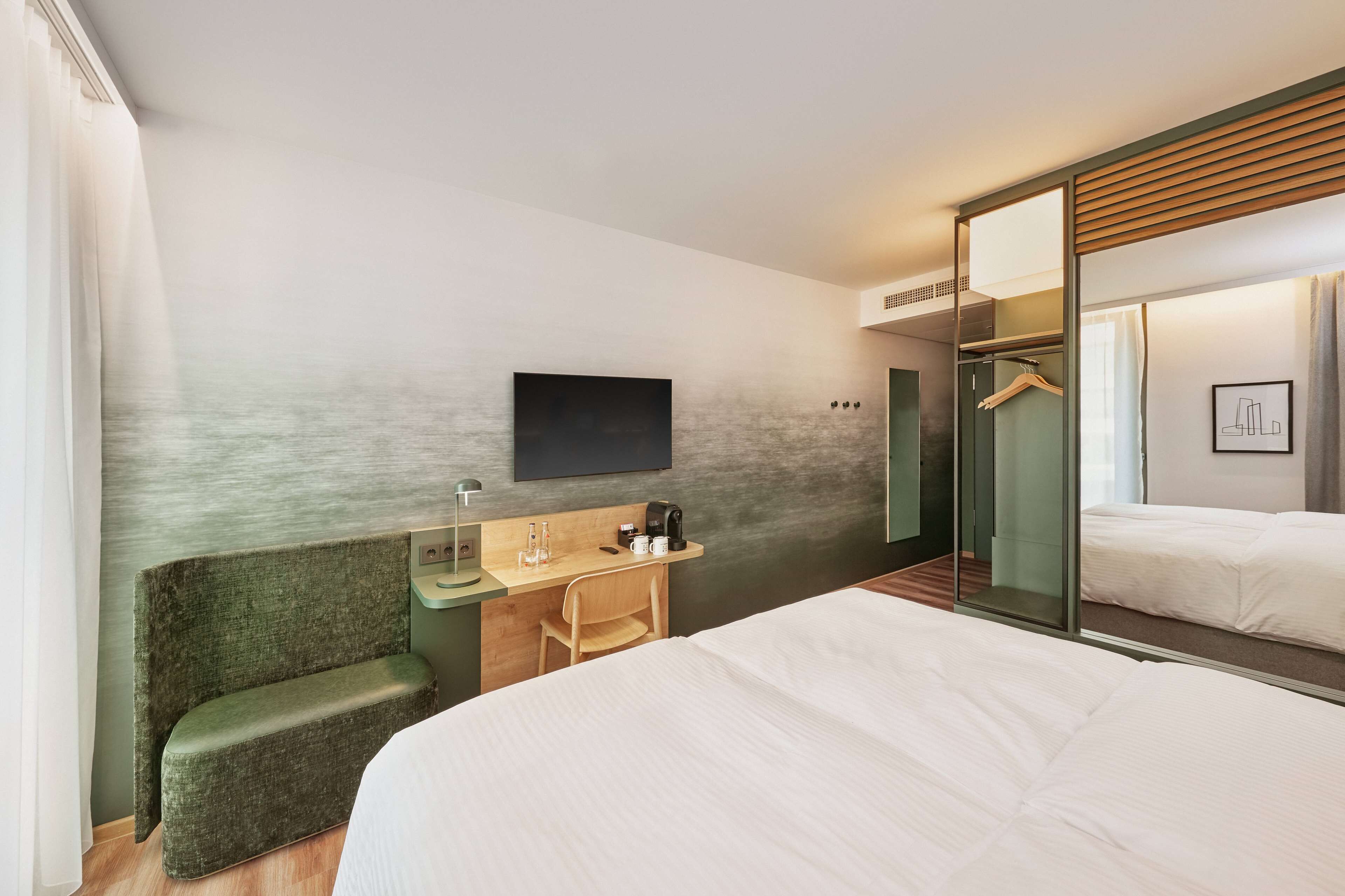 Een moderne hotelkamer met een groot bed, een bureau met stoel, een flatscreen televisie aan de muur, een spiegel en een inloopkast.