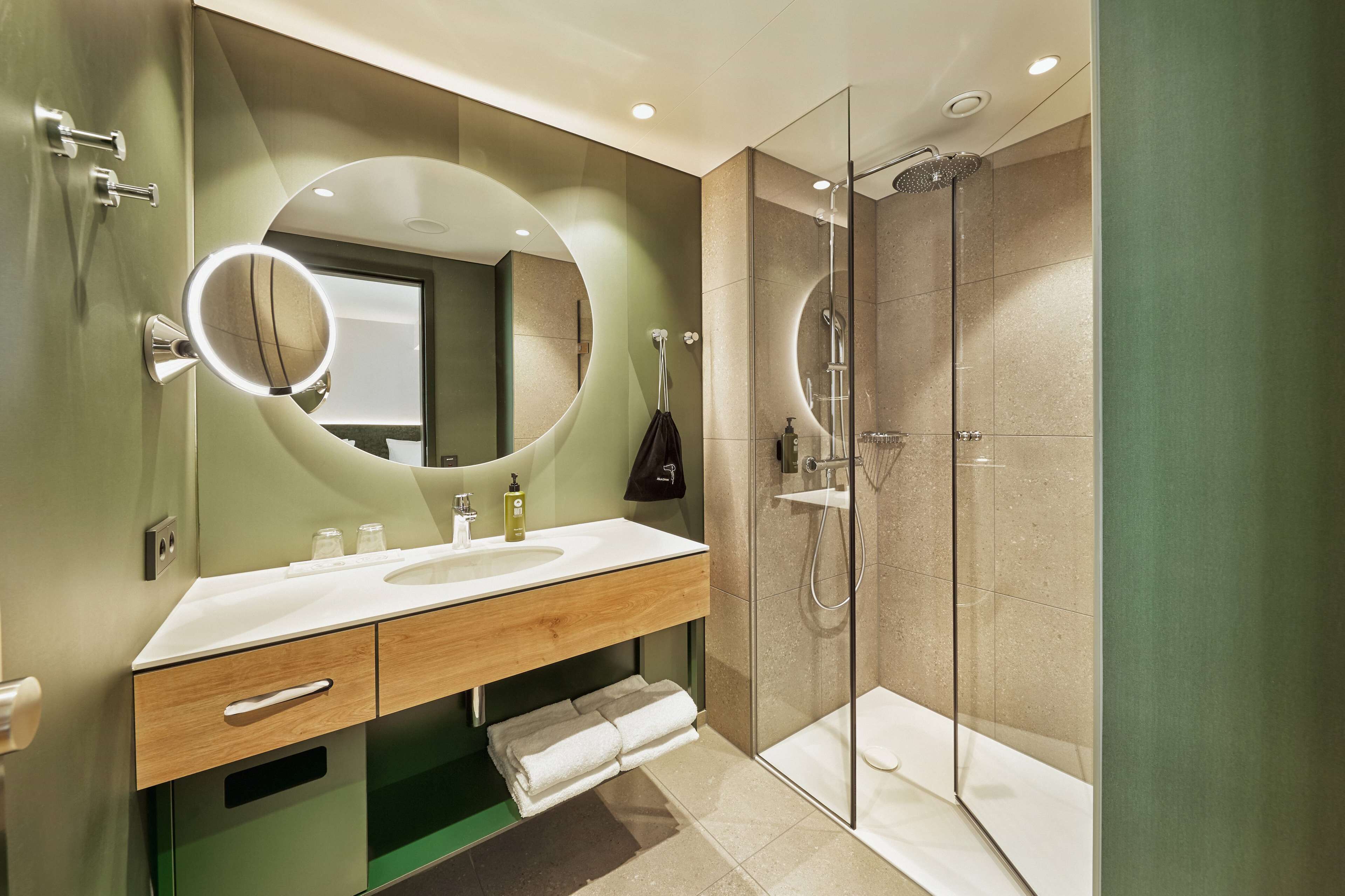 A modern bathroom with a large mirror, a sink, and a glass-enclosed shower.