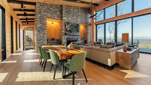 A spacious living area with a stone fireplace, a dining table with chairs, and a large window offering a view of the outdoors. - Blue Ridge Ultra Luxury with Stunning Mountain & Lake Views, Near Aska & Marina (Blue Ridge)