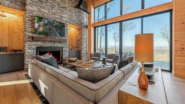 A modern living room with a stone fireplace, large windows, and a view of the outdoors. - Blue Ridge Ultra Luxury with Stunning Mountain & Lake Views, Near Aska & Marina (Blue Ridge)