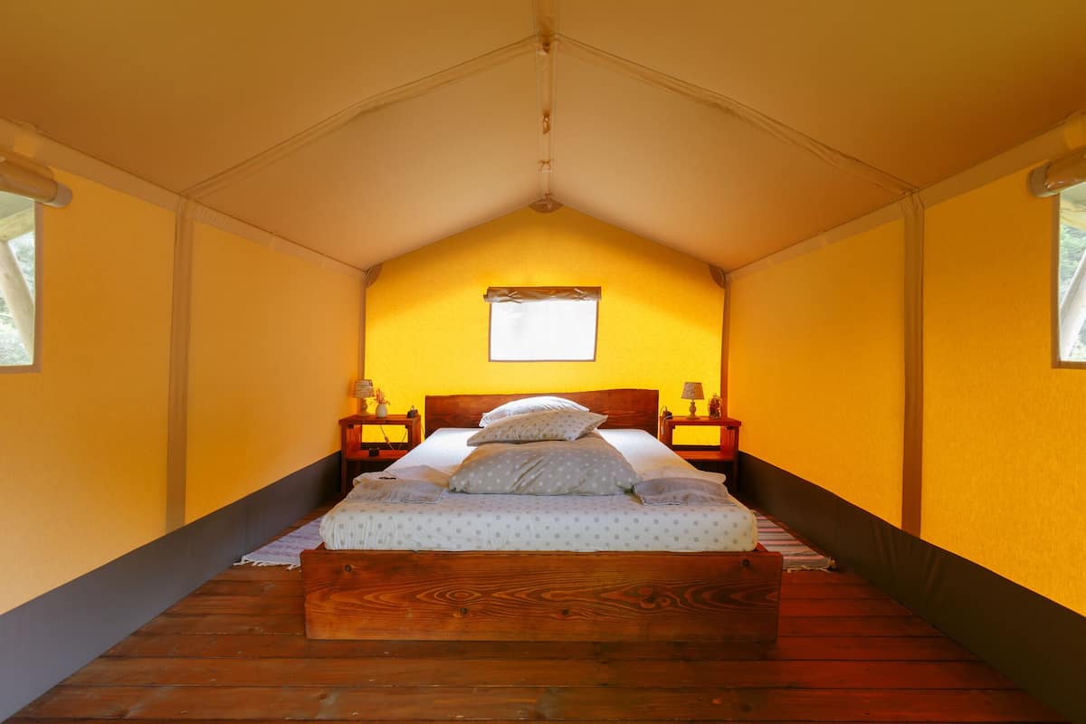 Una habitación con cama, suelo de madera, paredes amarillas y una ventana.