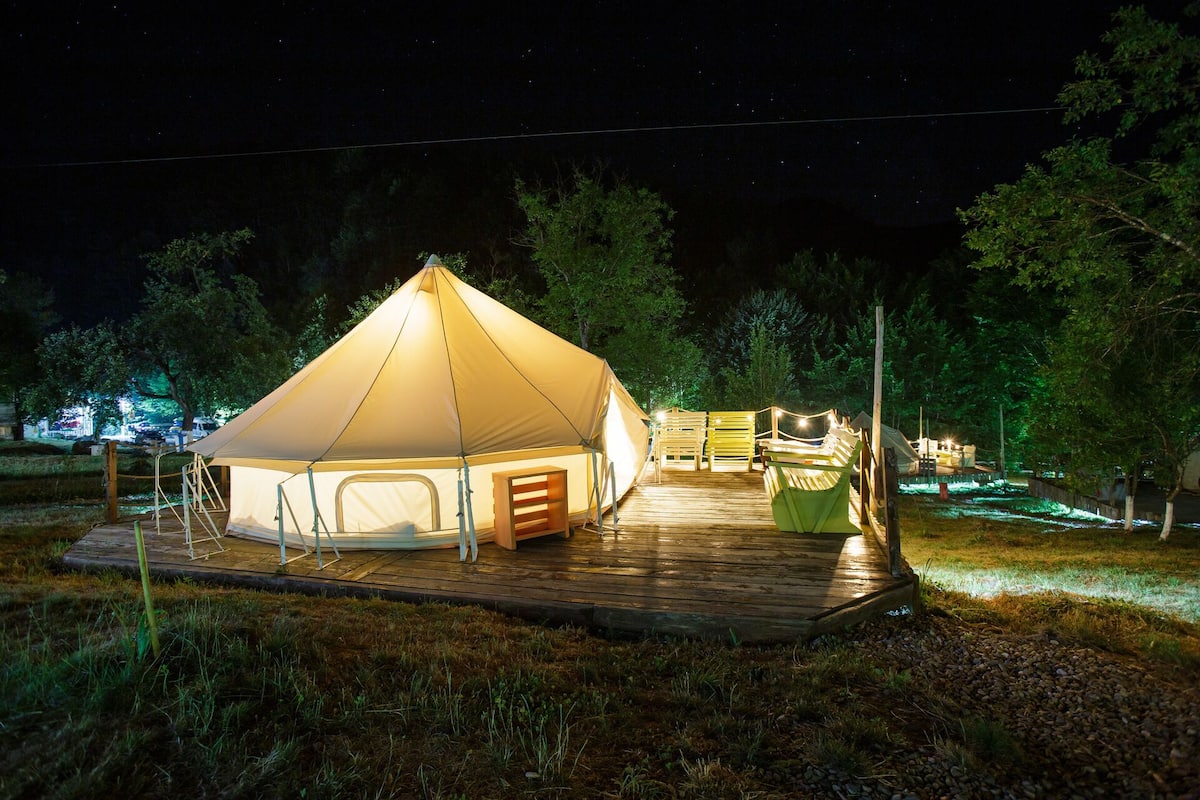 Una carpa grande y bien iluminada con un piso de madera y una pequeña construcción de madera cerca.