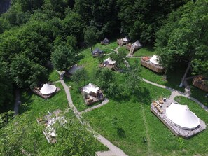 Vista aérea de un camping con varias tiendas de campaña y estructuras de madera, rodeado de vegetación densa.