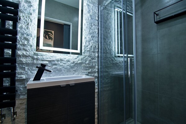 A modern bathroom with a stone wall, a glass shower enclosure, and a minimalist sink. - Bellerose 1 (Lancaster)
