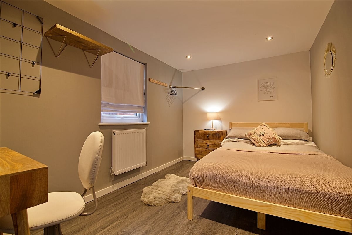 A bedroom with a bed, a chair, a desk, a radiator, and a window with blinds.
