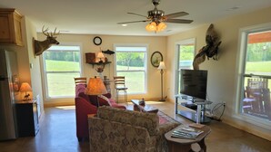 A spacious living room with a red sofa, patterned armchair, and a coffee table. A ceiling fan and a mounted deer head are visible. - Lake Cabin near the Bourbeuse River (Leslie)