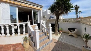Une maison dotée d’un patio couvert, d’un escalier et de plantes en pot.
