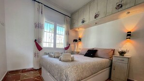 Une chambre à coucher avec un lit, une table de chevet, une armoire et une fenêtre avec des rideaux.