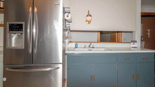 A kitchen with a stainless steel refrigerator, a built-in water dispenser, and a sink with a blue cabinet below. - Waters Edge Cottage (Merrimac)