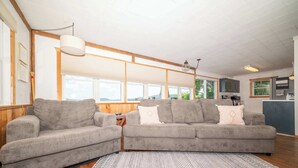 A living room with two grey sofas, a patterned rug, and a kitchen in the background. - Waters Edge Cottage (Merrimac)