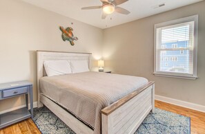 Ein Schlafzimmer mit Bett, Nachttisch, Schreibtisch, Deckenventilator, einem Fenster mit Jalousien und einer Wanddekoration.