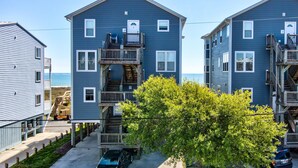 Un edificio residencial frente al mar con varios balcones, una terraza de madera y vistas al océano.