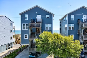 Un edificio residencial frente al mar con varios balcones, una terraza de madera y vistas al océano.