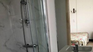 A bathroom with a glass-enclosed shower, a sink with a mirror, and a bed in the background. - Pretty F2 1 to 4 persons 2 (L'Aiguillon-la-Presqu'île)