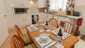 Une cuisine moderne avec des meubles blancs, un four à micro-ondes, une cuisinière et un évier. On y trouve une table à manger mise avec des assiettes, des verres et des couverts.
