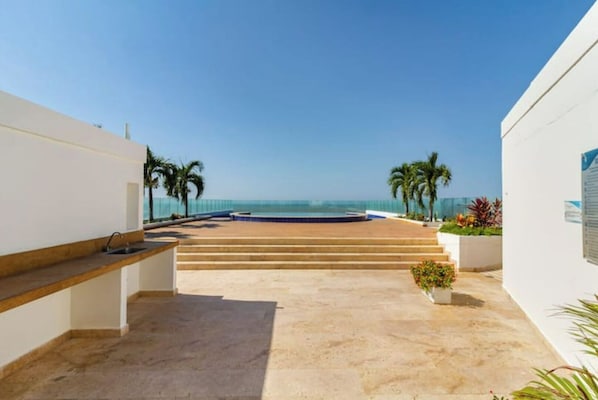 A modern outdoor area with a pool, palm trees, and a clear view of the ocean. - Beachfront Apartment! (Cartagena de Indias)