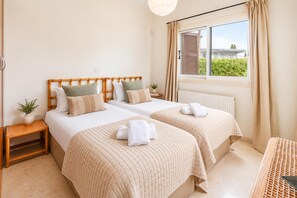 A hotel room with two beds, a window with curtains, a bedside table with a plant, and a radiator. - Villa Demiana by Ezoria Villas (Coral Bay)