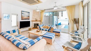 Ein Wohnzimmer mit Fernseher, einer Couch, Sesseln, einem Kamin und Blick auf einen Pool.