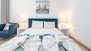 Ein Hotelzimmer mit einem Bett, zwei Nachttischlampen, einem Segelbootgemälde, einem blauen Kopfteil und einem blauen Sofa mit Kissen.
