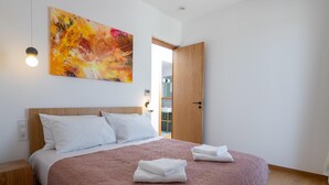 A bedroom with a bed, a painting, a door, and a bedside table. - Nisi Living Concept - Rhodes Villa (Ialysos)