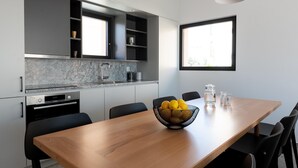A modern kitchen with built-in appliances, a dining table with chairs, and a window providing natural light. - Nisi Living Concept - Rhodes Villa (Ialysos)