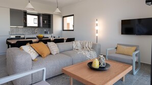 A modern living room with a grey sofa, a wooden coffee table, and a TV mounted on the wall. - Nisi Living Concept - Rhodes Villa (Ialysos)