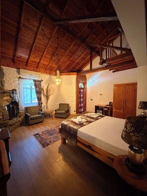A spacious room with a large bed, a stone fireplace, a wooden ceiling, and a cozy seating area. - Tlos Butik Otel (Seydikemer)