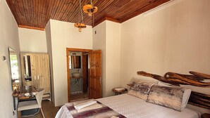 A bedroom with a wooden ceiling, a bed with a patterned bedspread, a wooden headboard, and a small bedside table.