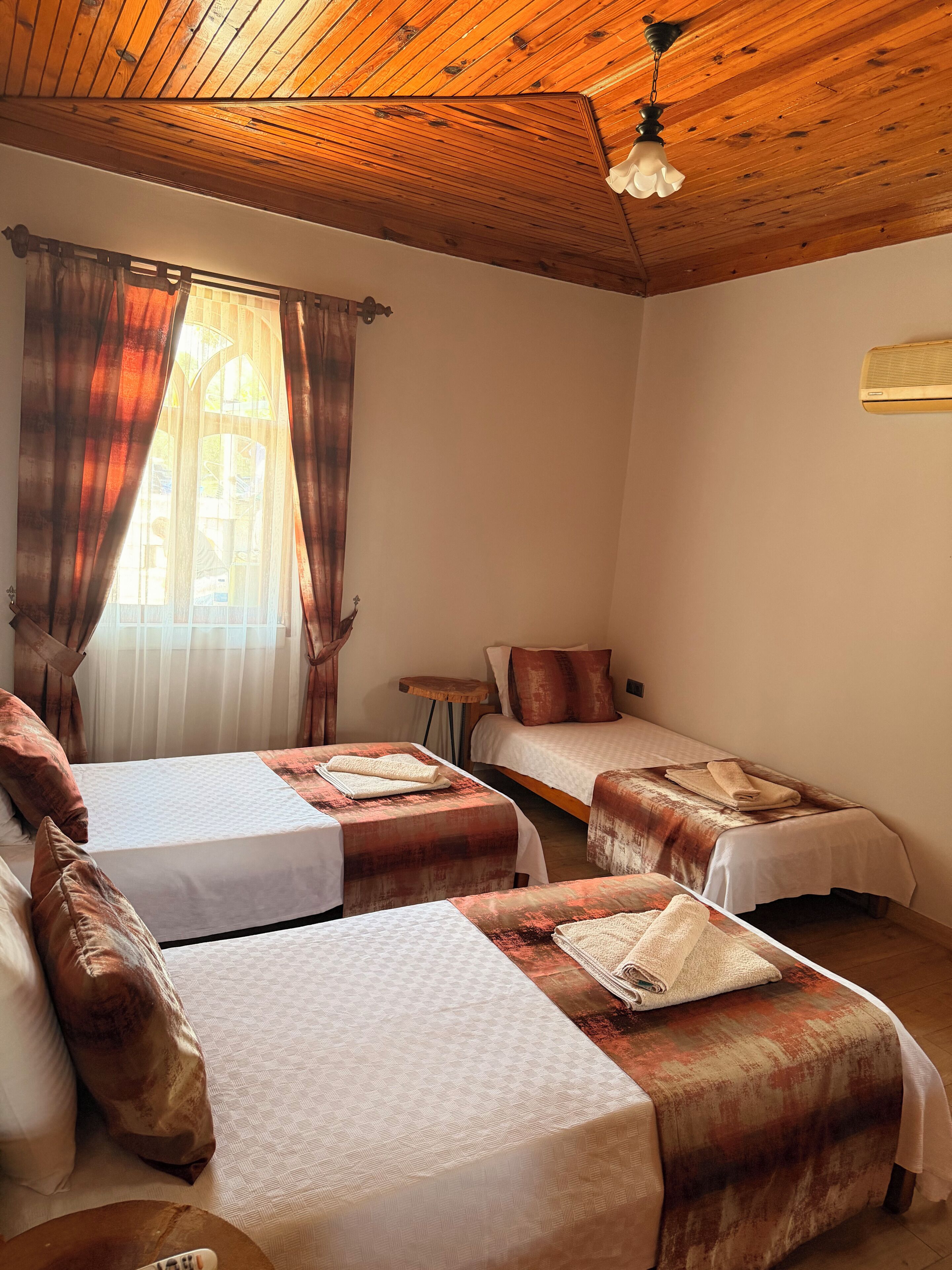 A room with two beds, a ceiling fan, and a window with curtains.
