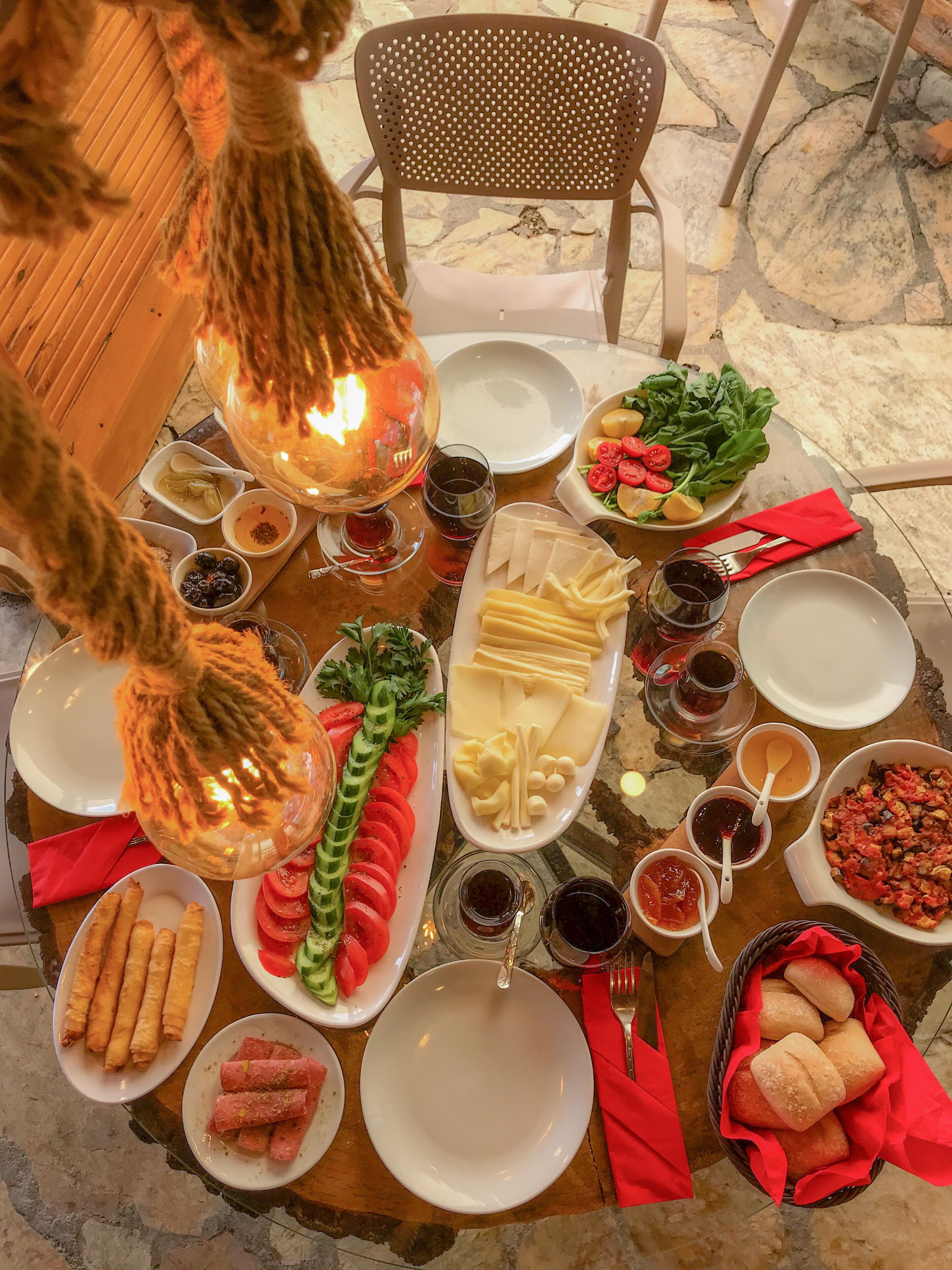 A table set with various dishes, including sliced tomatoes, cheese, and bread, with a chair and a decorative light fixture.