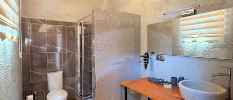 A bathroom with a wooden ceiling, a large mirror, a stone sink, and a glass shower enclosure.