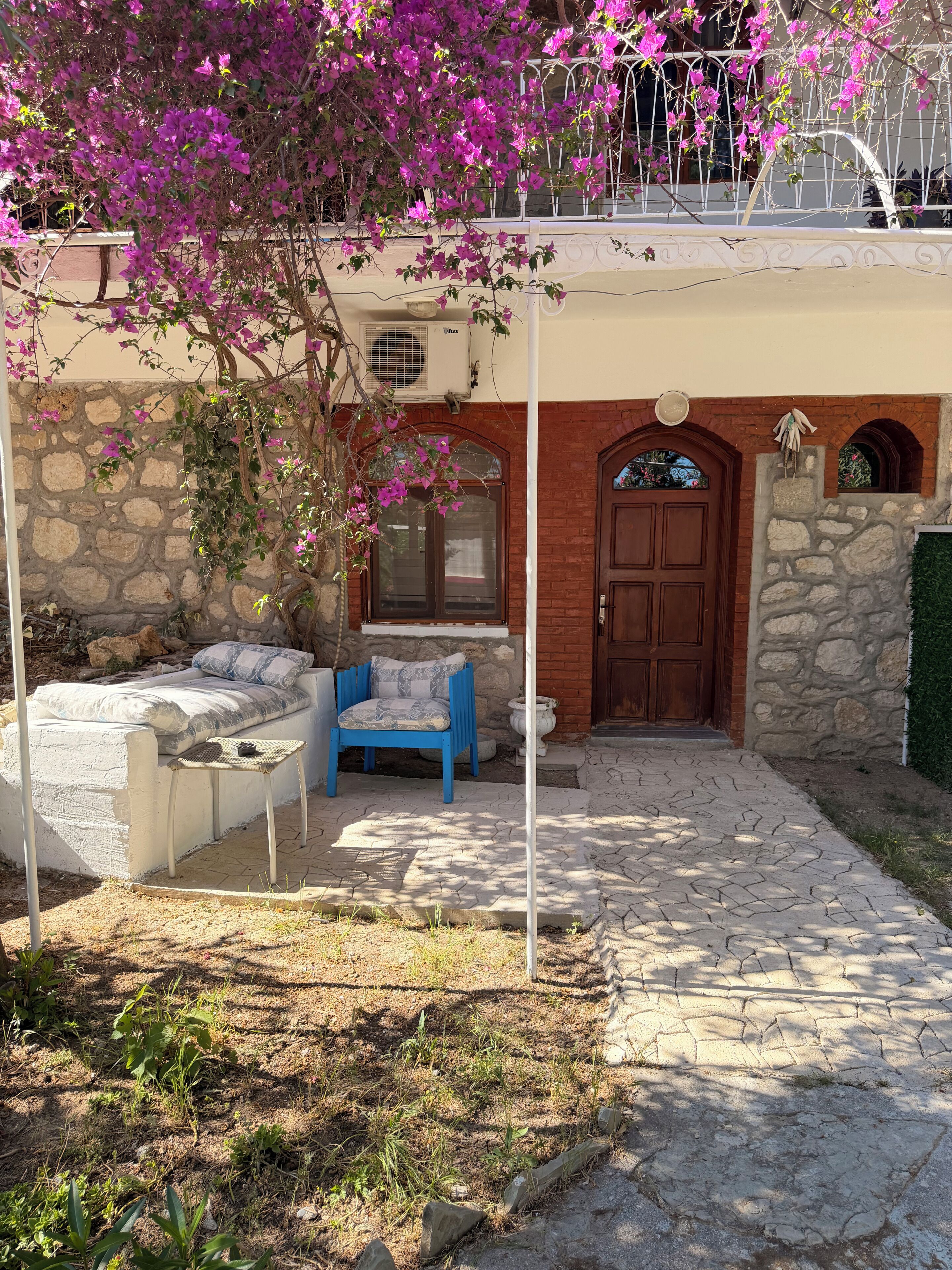 Un espacio de estar al aire libre techado, con pared de piedra, puerta de madera y una ventana.