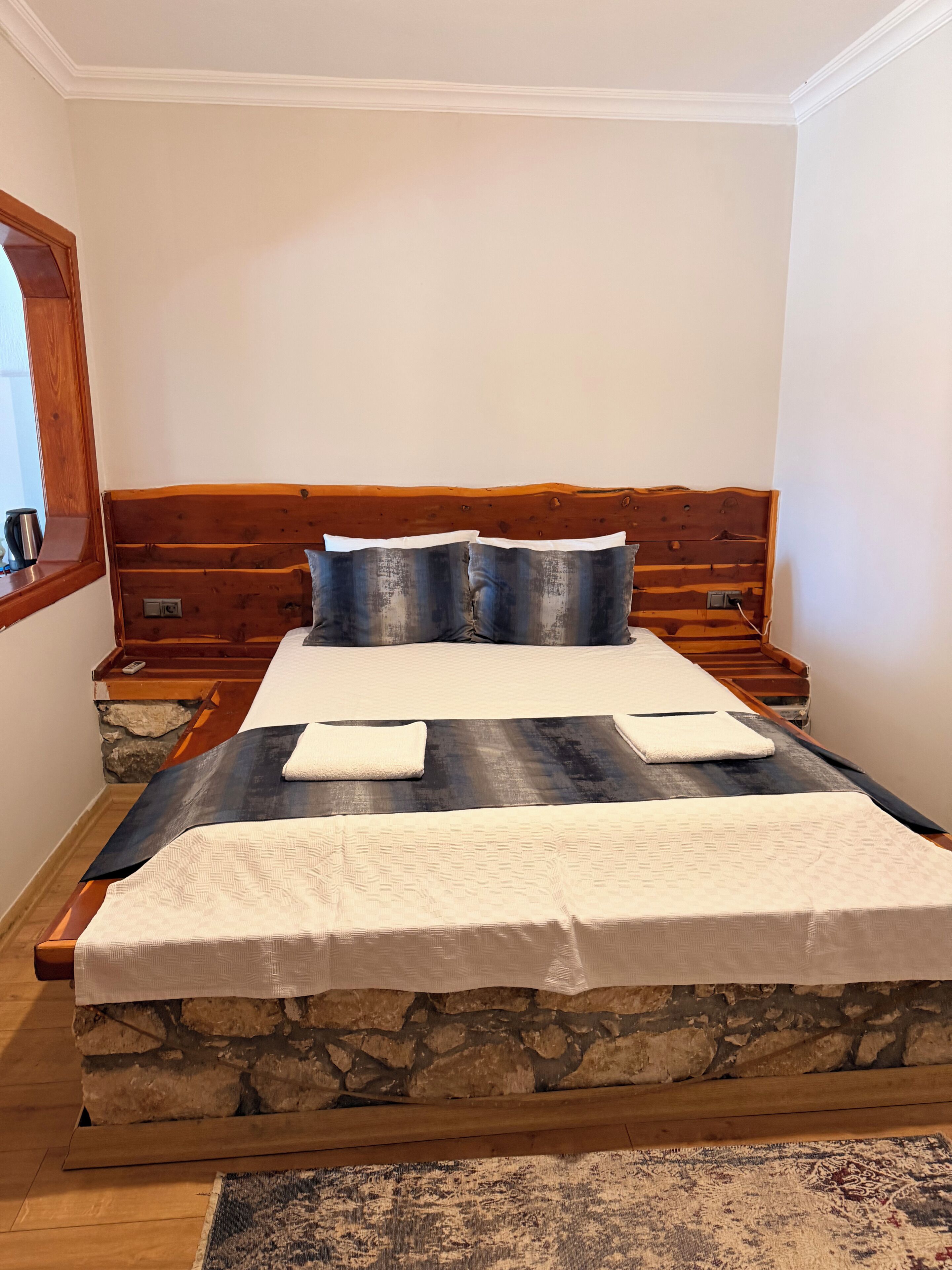 A double bed with a stone headboard, two nightstands, and a large window.