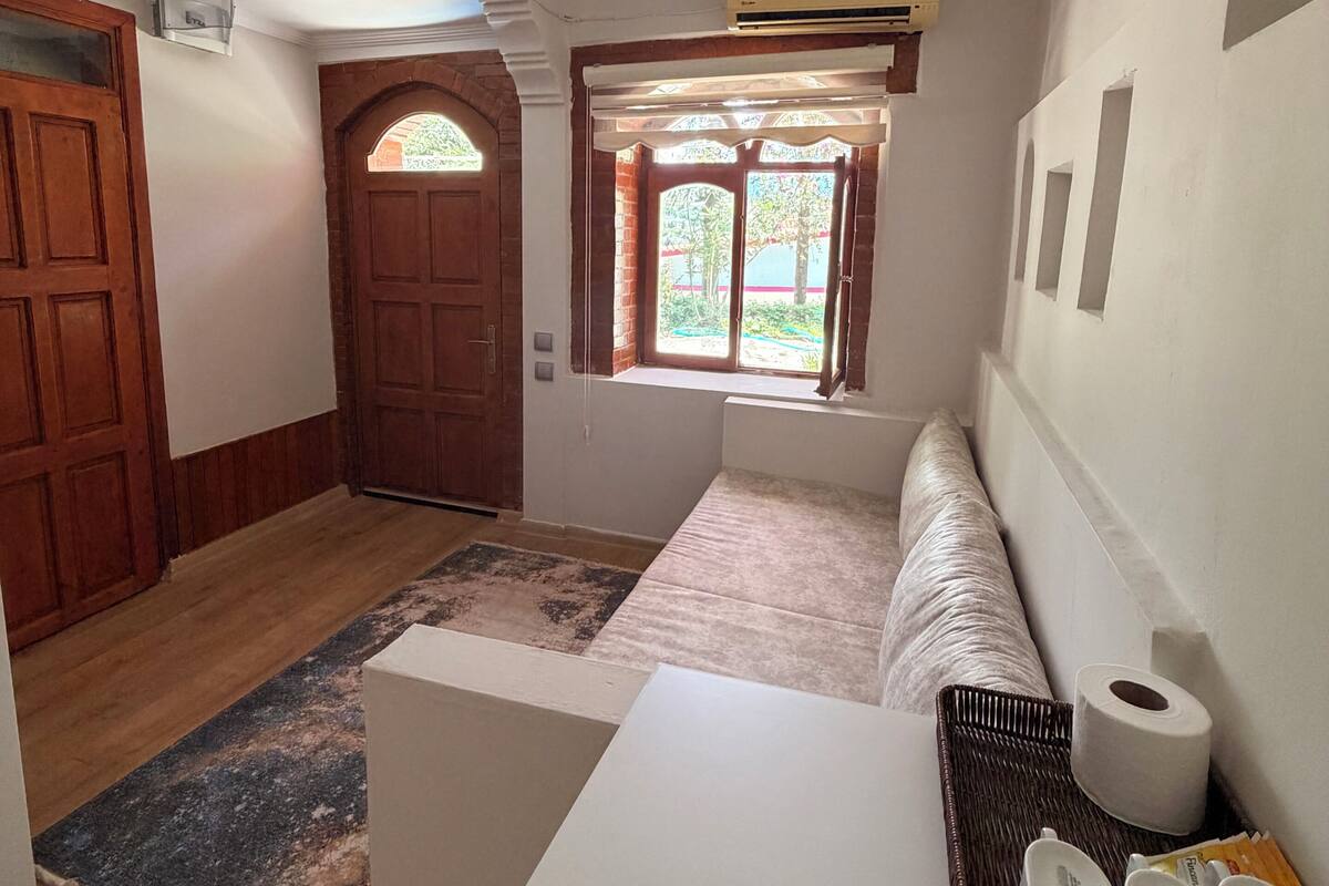 Ein Zimmer mit Holztür, einem Fenster mit Blick, einer Deckenleuchte und einer Wand-Klimaanlage.