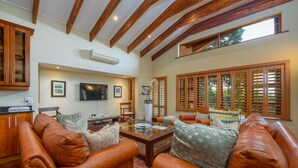 A spacious living room with leather sofas, a coffee table, and wooden shutters.