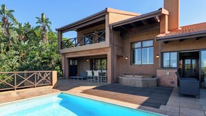 A two-story house with a swimming pool, outdoor seating, and a hot tub.