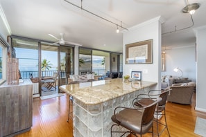A modern kitchen with a large island, bar stools, and a view of the ocean. - Koa Lagoon- Beachfront - Spectacular Location with Incredible Views (KIHEI)