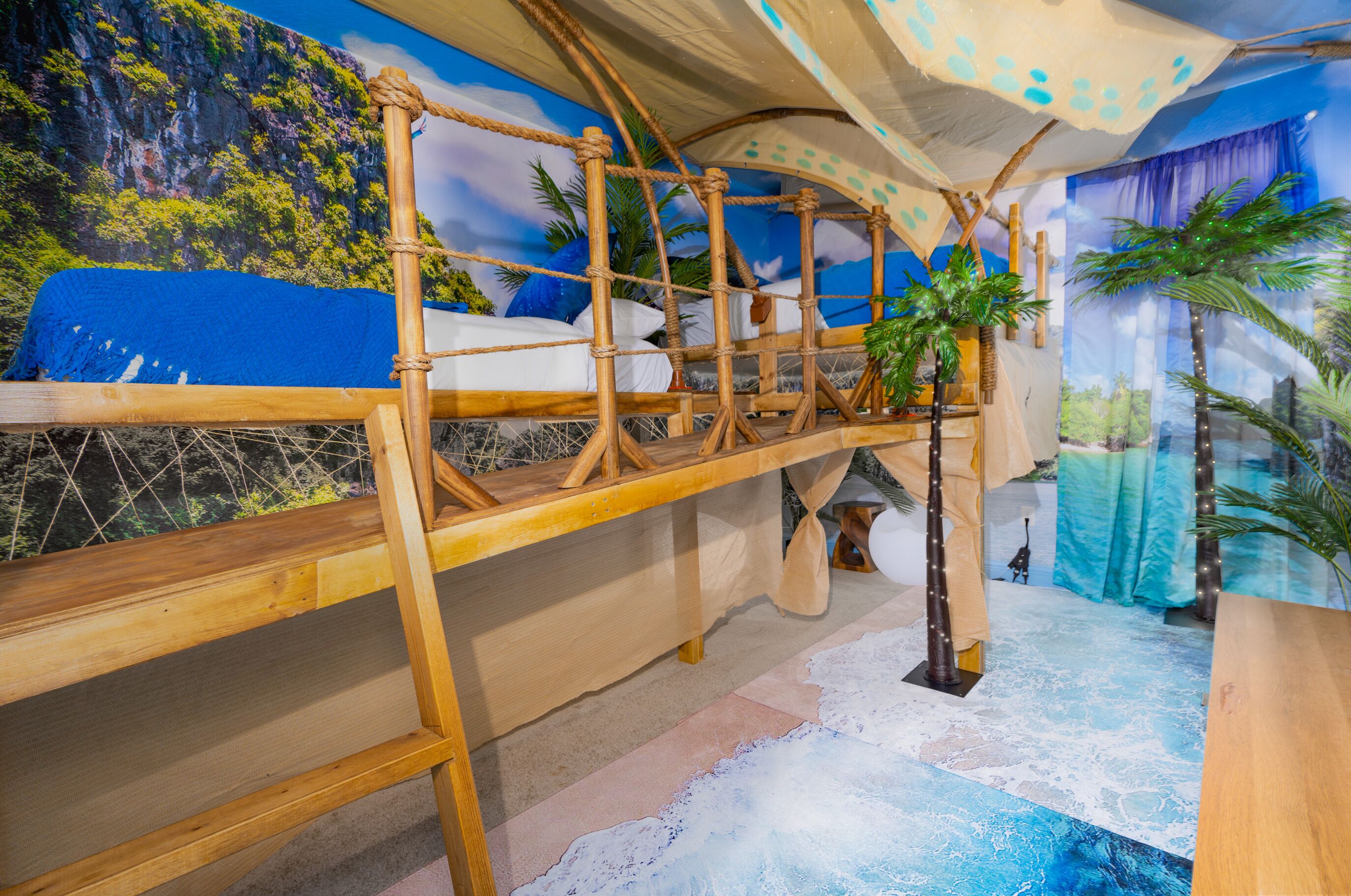 A room with a wooden bunk bed, a small table, and a mural of a tropical landscape.