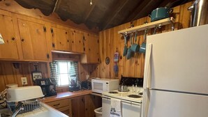 Une cuisine avec des meubles de rangement en bois, un évier blanc, une cuisinière, un four à micro-ondes et un réfrigérateur.