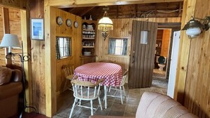 Interior acogedor de una cabaña con comedor que incluye una mesa y sillas a cuadros, un sofá y techo de madera.