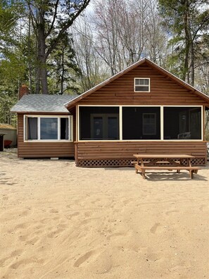 A wooden cabin with a large window and a picnic table in front.
