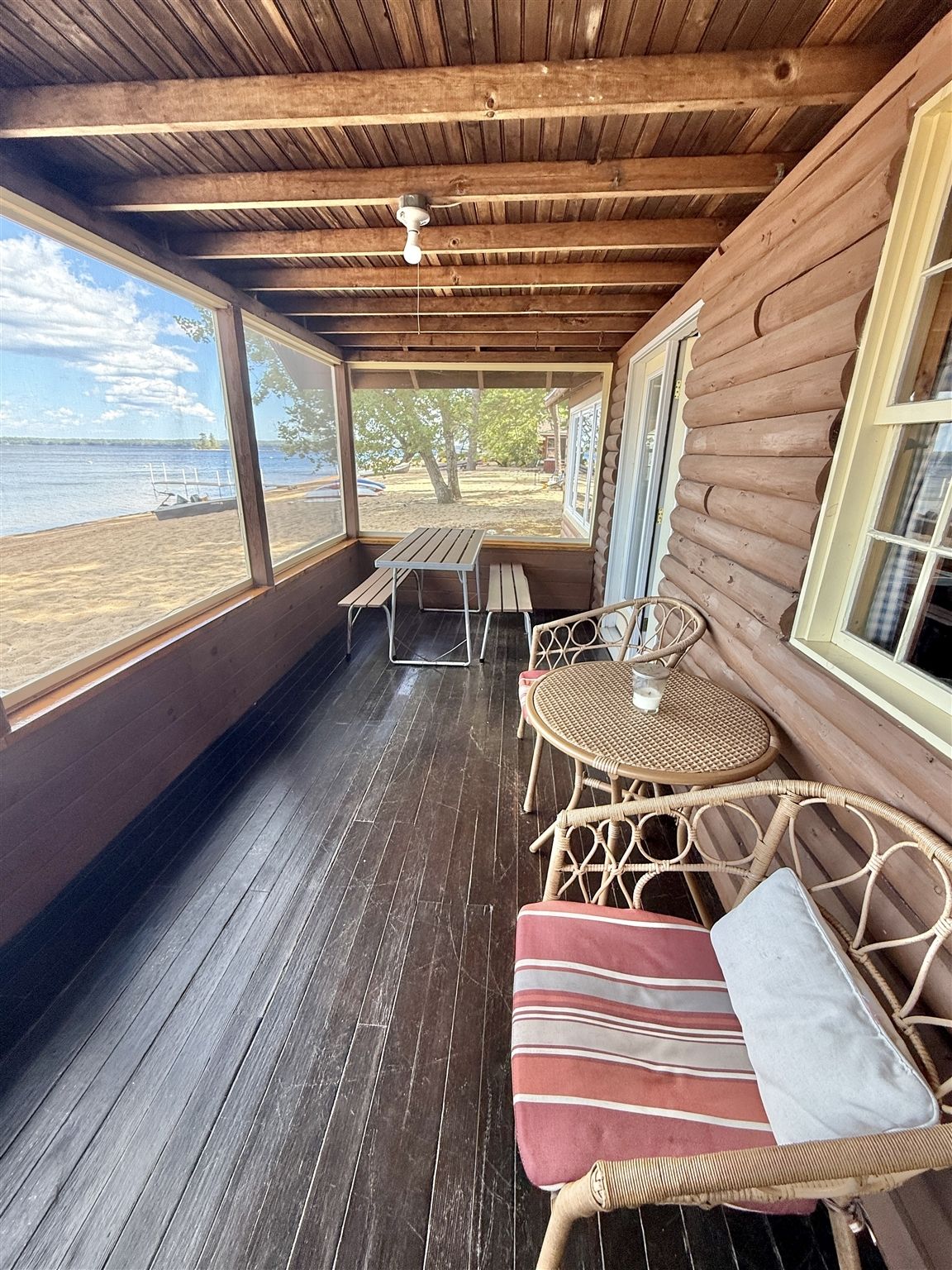 A wooden deck with a table and chairs, overlooking a beach.