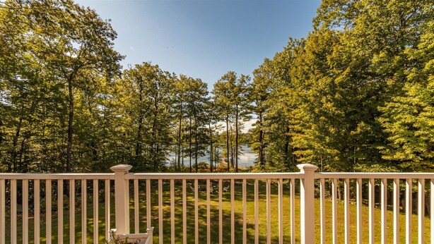 A wooden deck with a white railing, overlooking a grassy area with trees and a body of water in the background. - WATERFRONT ON LONG LAKE  (HARRISON)