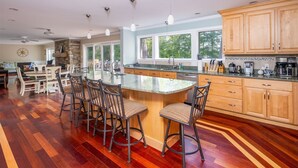 A spacious kitchen with a large island, wooden cabinets, and a stone accent wall. - WATERFRONT ON LONG LAKE  (HARRISON)