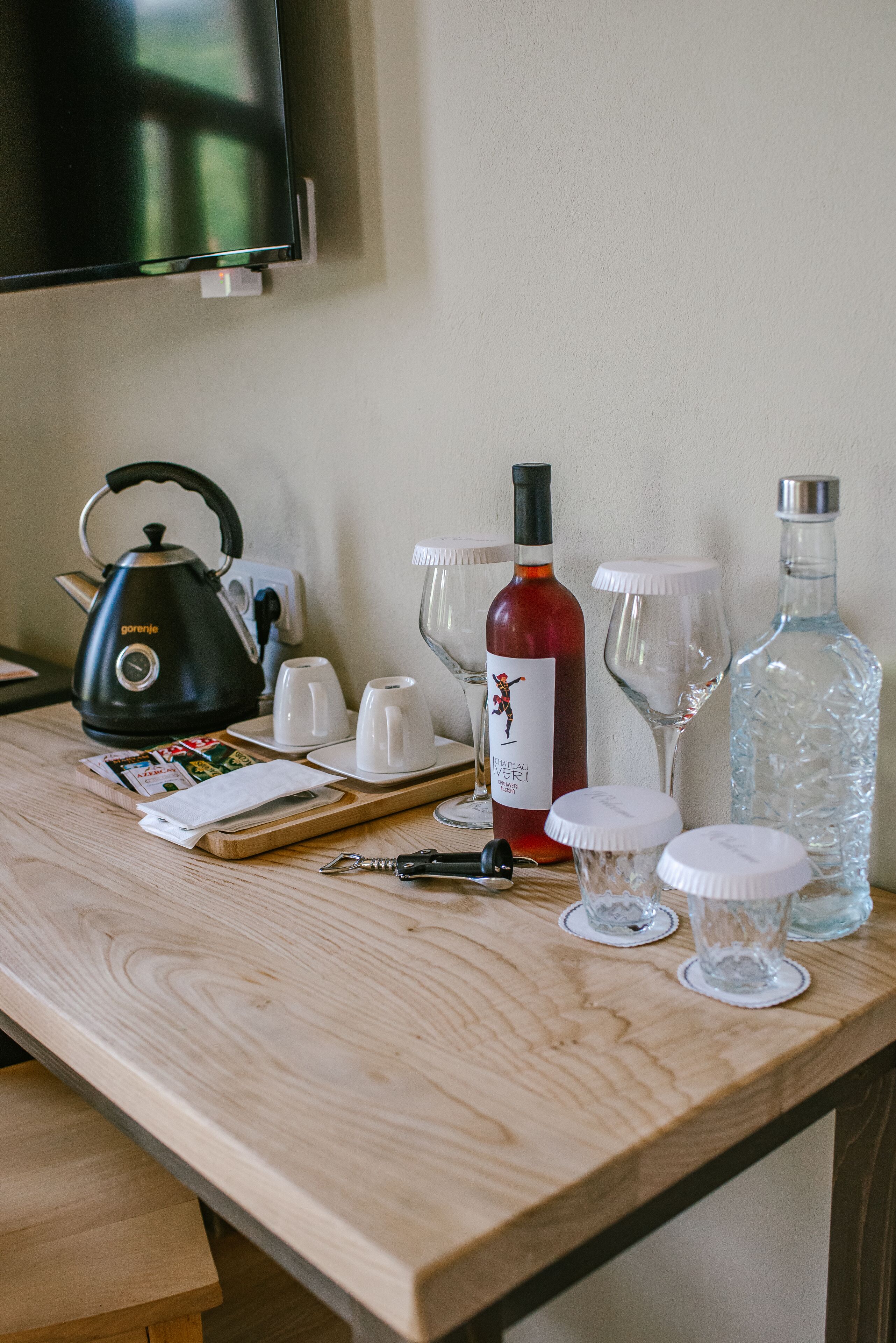 A wooden table with a kettle, wine bottle, glasses, and a bottle of water.